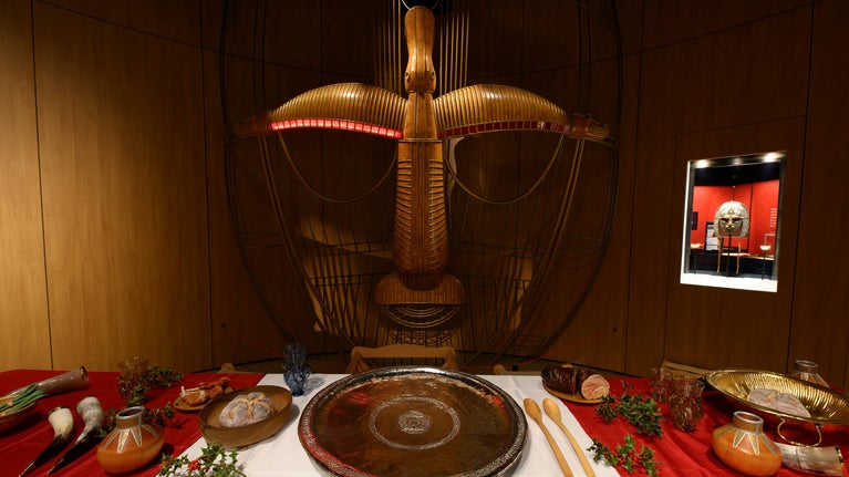 The feasting table decorated with drinking horns and food all positioned under a sculpture of the famous Sutton Hoo helmet
